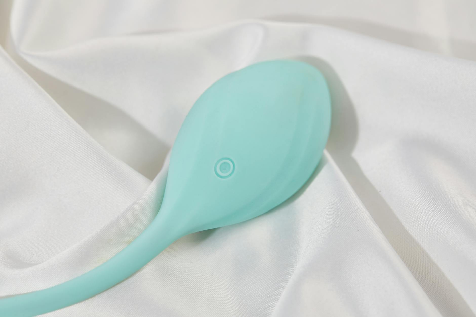 A stylish teal lemon clitoral vibrator on smooth white silk fabric, symbolizing self-care and solo pleasure after divorce.