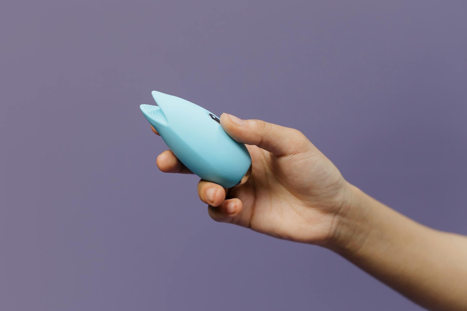 A blue silicone vibrator held gently in hand against a calm purple background, symbolizing first-time exploration of pleasure